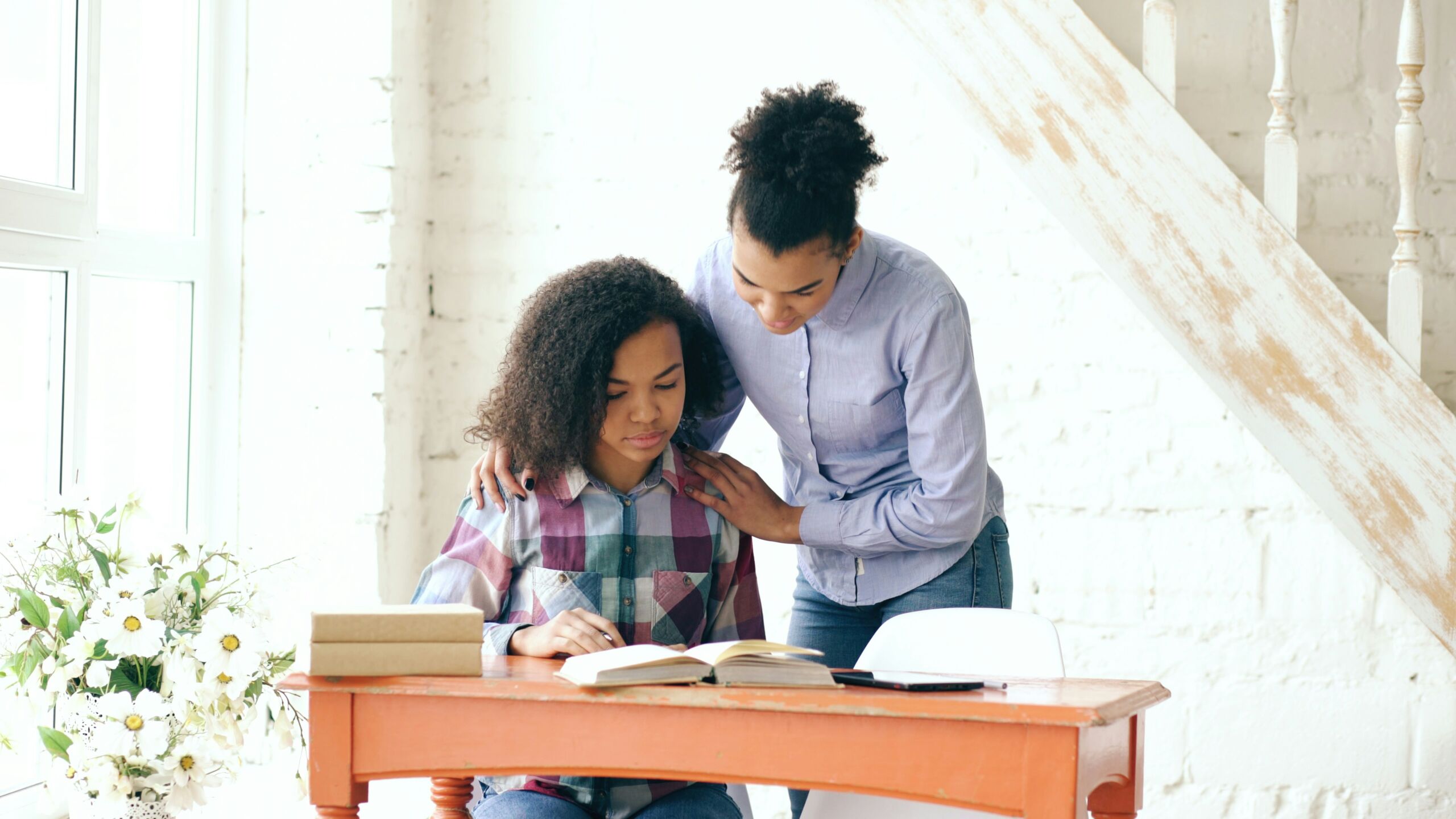 Adult standing behind a child with a hand on their shoulder while the child reads at a desk